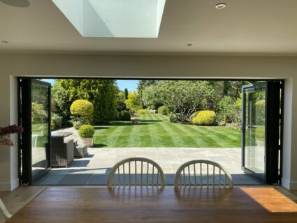 view of a new extension with black bifolds and a large garden lawn
